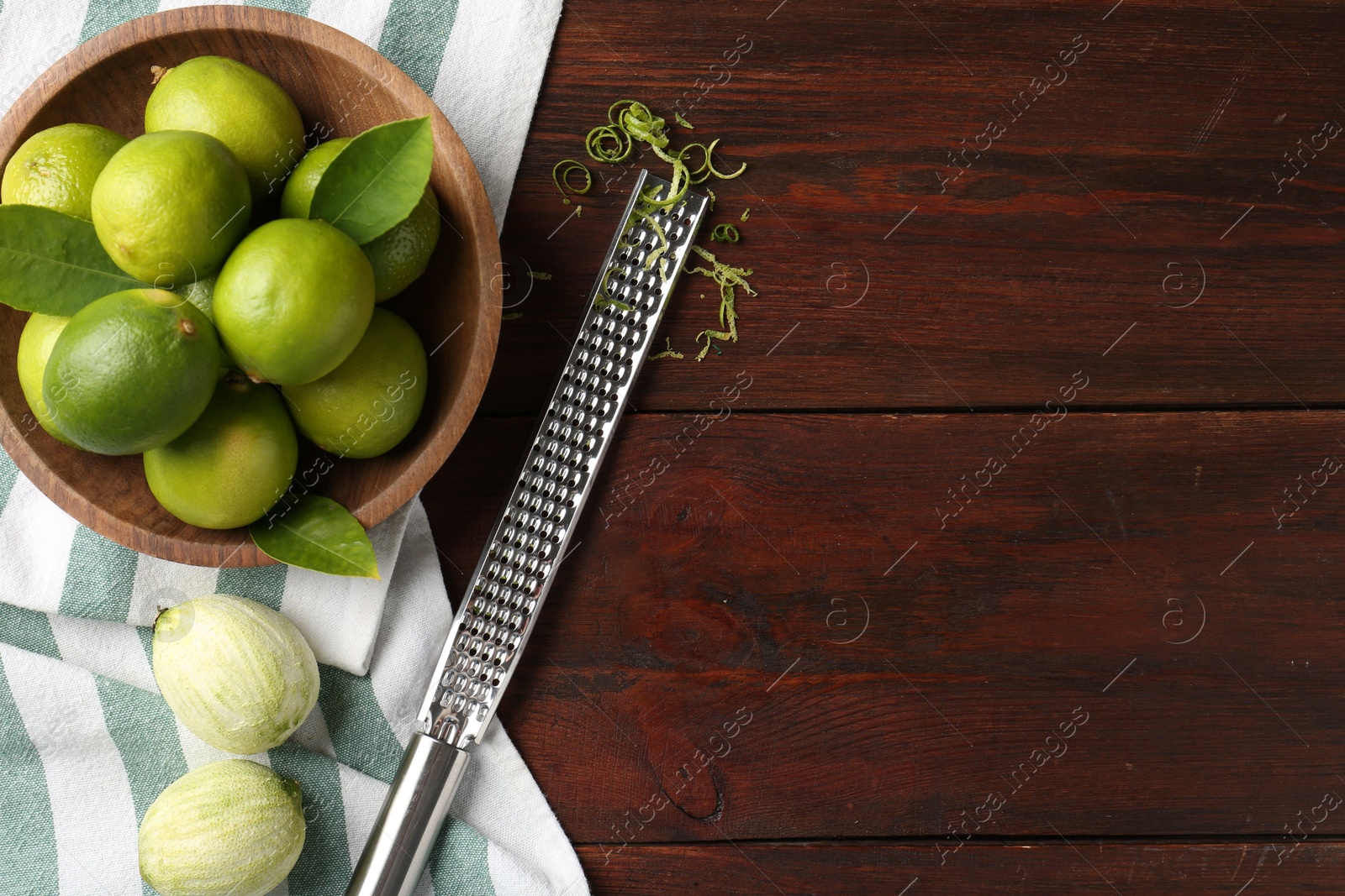 Photo of Lime zest, grater and fresh fruits on wooden table, flat lay. Space for text