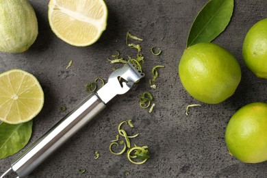 Photo of Lime zest, zester, fresh fruits and leaves on grey textured table, flat lay