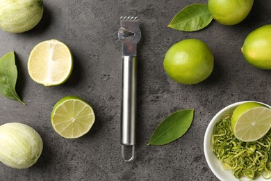 Photo of Lime zest, fresh fruits and zester on grey textured table