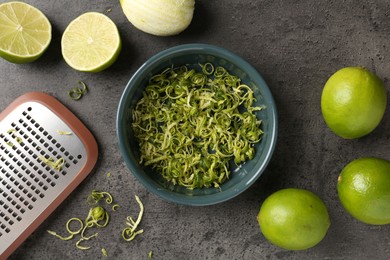 Photo of Lime zest, fresh fruits and grater on grey textured table