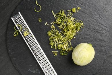 Photo of Lime zest, grater and peeled fruit on dark textured table, top view