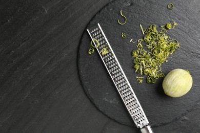 Photo of Lime zest, grater and peeled fruit on dark textured table, top view. Space for text