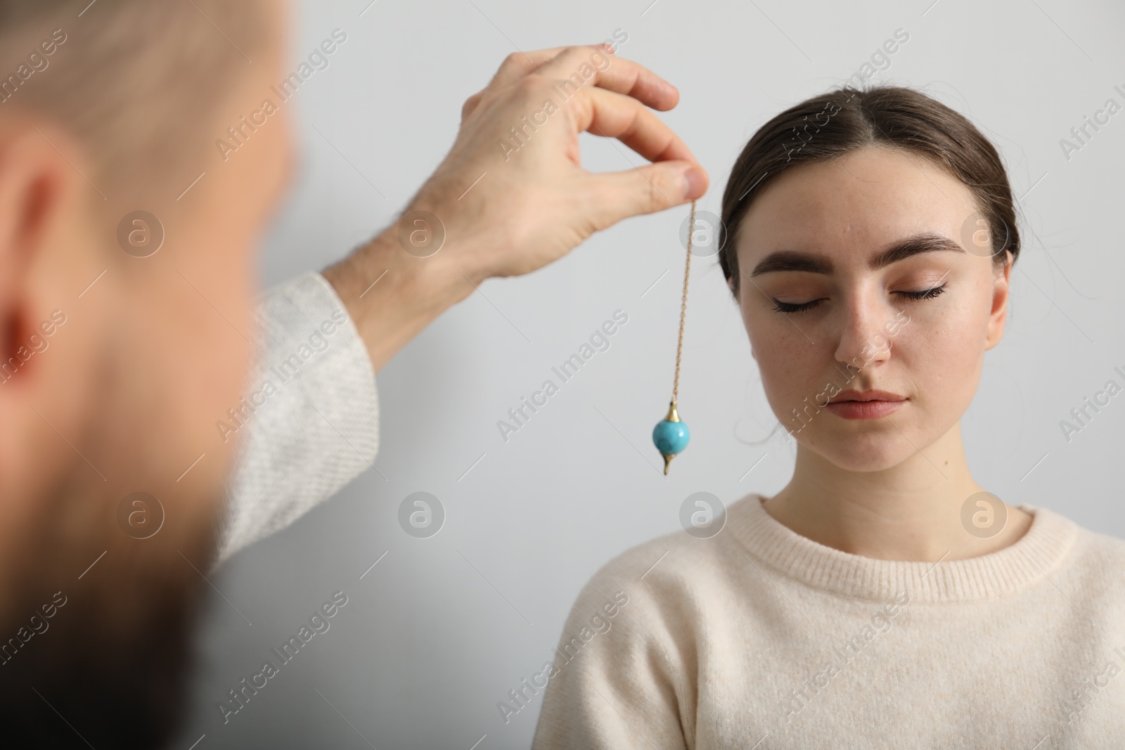 Photo of Psychologist using pendulum while working with patient during hypnosis session indoors, closeup