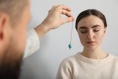 Photo of Psychologist using pendulum while working with patient during hypnosis session indoors, closeup