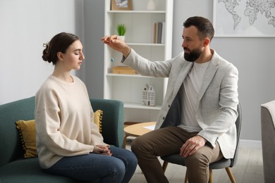 Photo of Psychologist using pendulum while working with patient during hypnosis session indoors