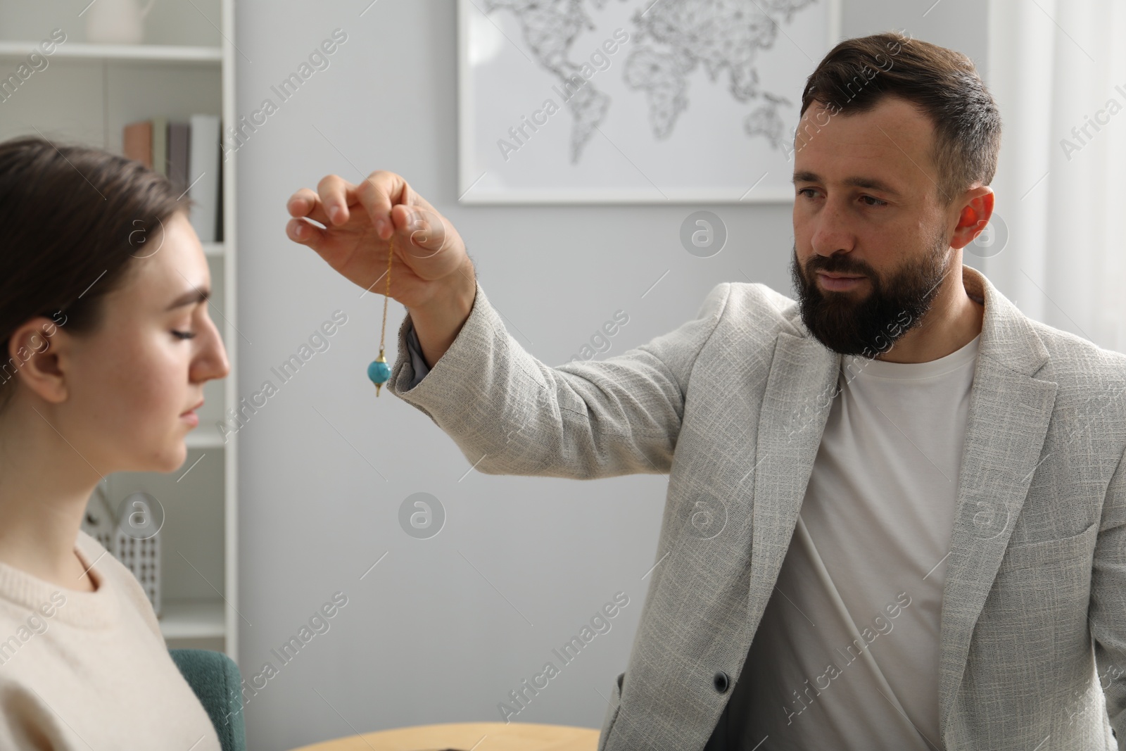 Photo of Psychologist using pendulum while working with patient during hypnosis session indoors