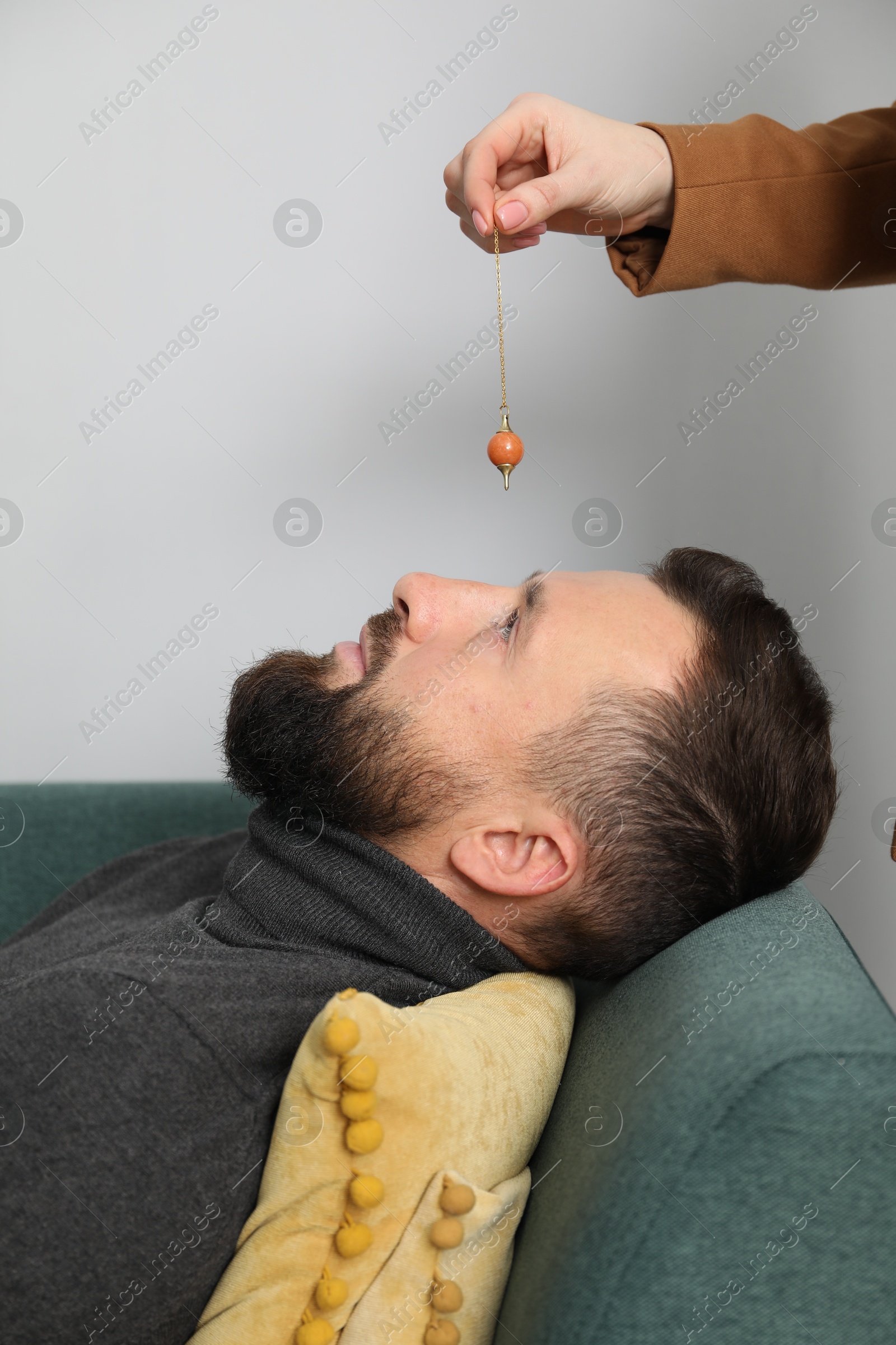 Photo of Psychologist using pendulum while working with patient during hypnosis session indoors, closeup