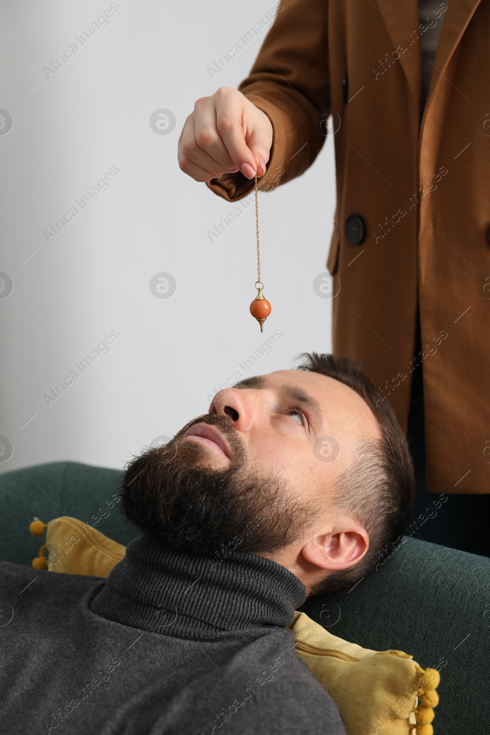 Photo of Psychologist using pendulum while working with patient during hypnosis session indoors, closeup