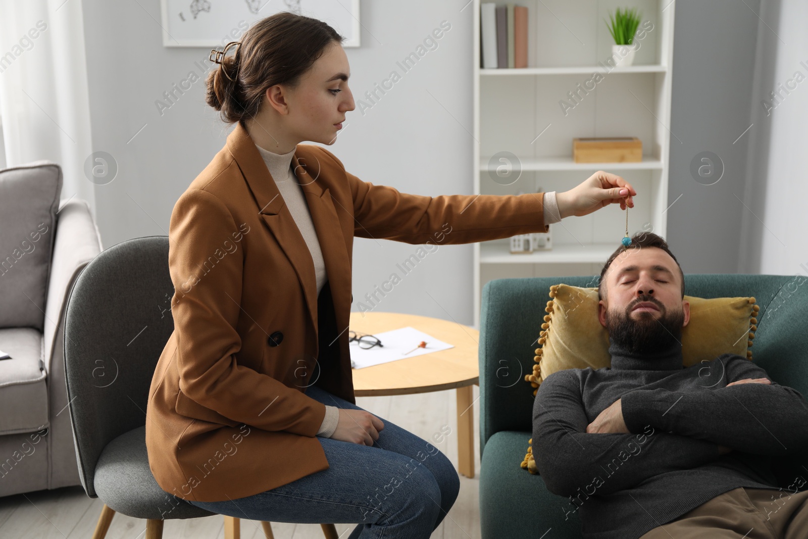 Photo of Psychologist using pendulum while working with patient during hypnosis session indoors