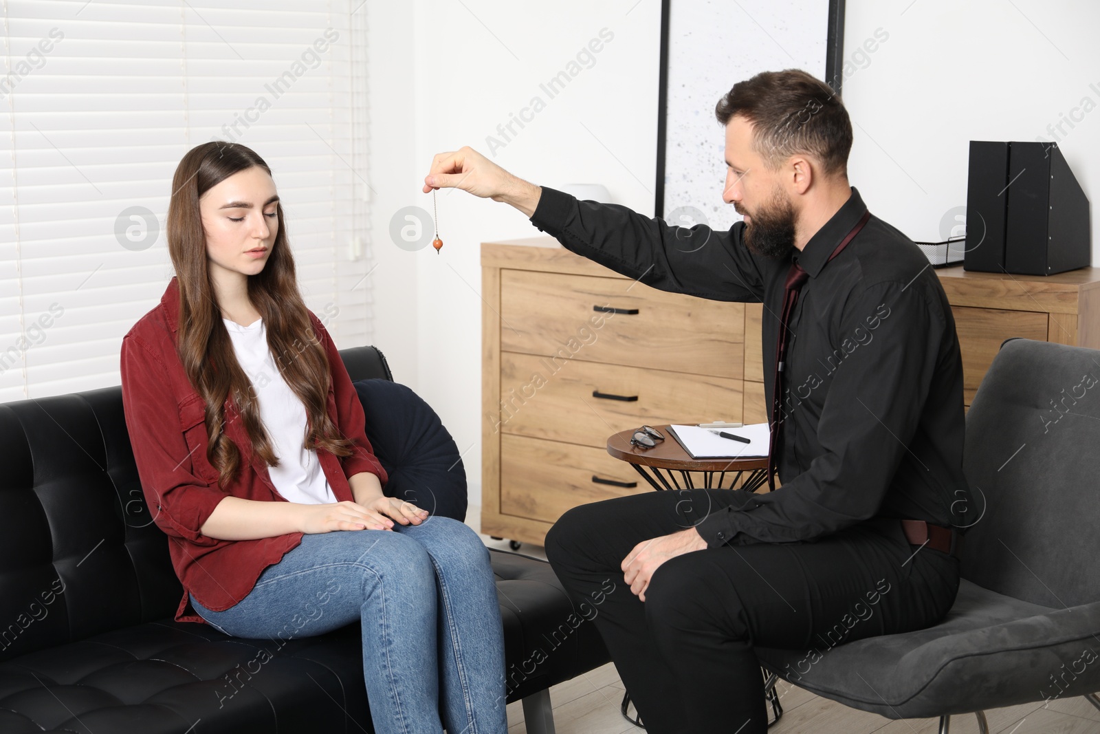 Photo of Psychologist using pendulum while working with patient during hypnosis session indoors