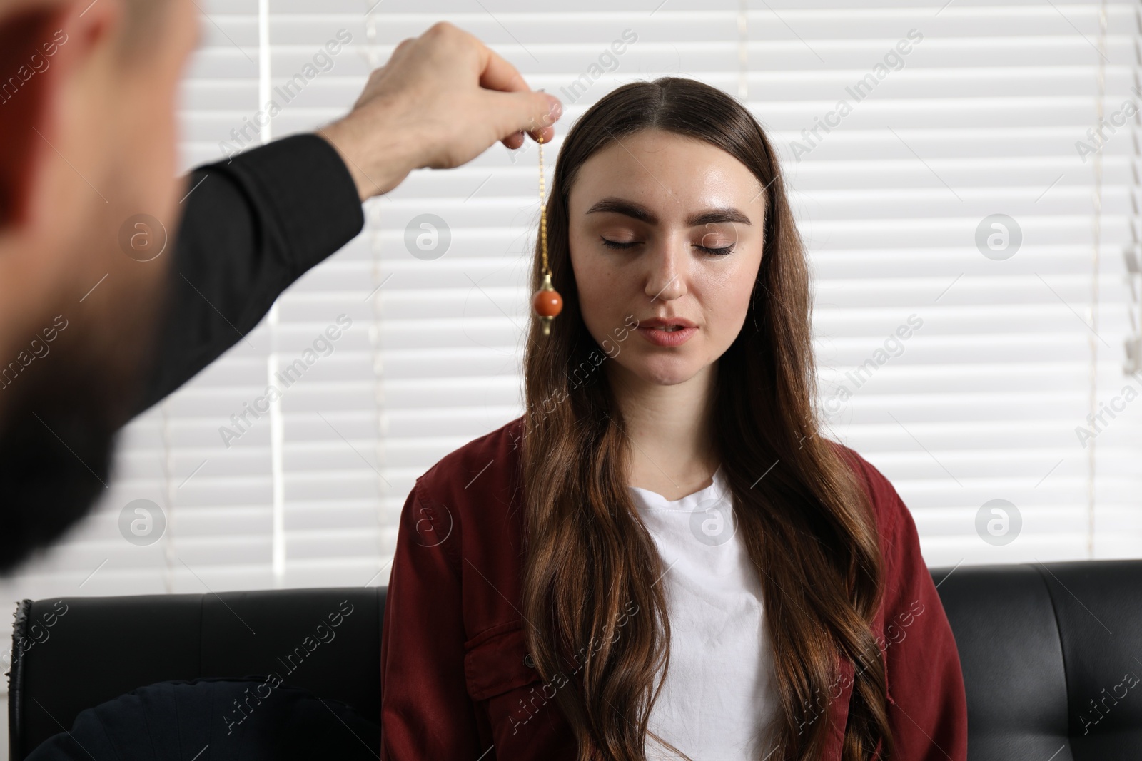 Photo of Psychologist using pendulum while working with patient during hypnosis session indoors, closeup