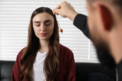 Photo of Psychologist using pendulum while working with patient during hypnosis session indoors, closeup