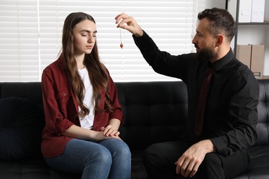 Photo of Psychologist using pendulum while working with patient during hypnosis session indoors