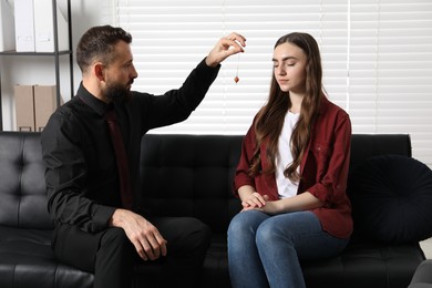 Photo of Psychologist using pendulum while working with patient during hypnosis session indoors