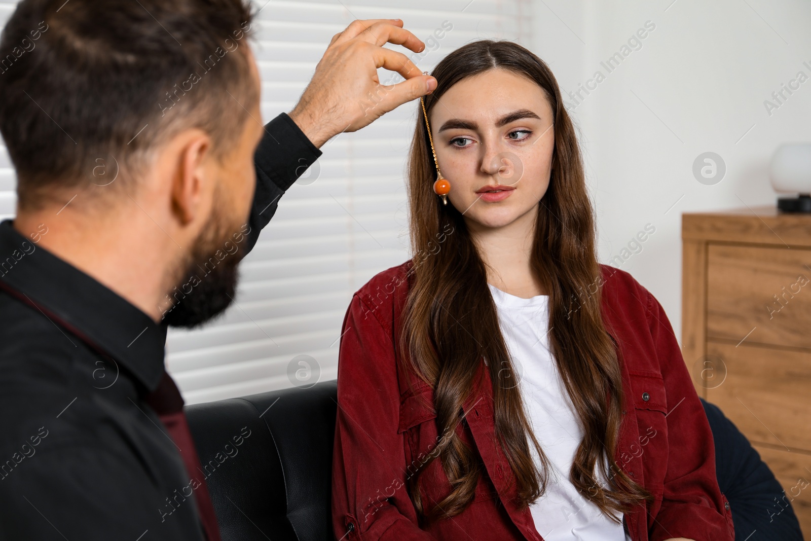 Photo of Psychologist using pendulum while working with patient during hypnosis session indoors