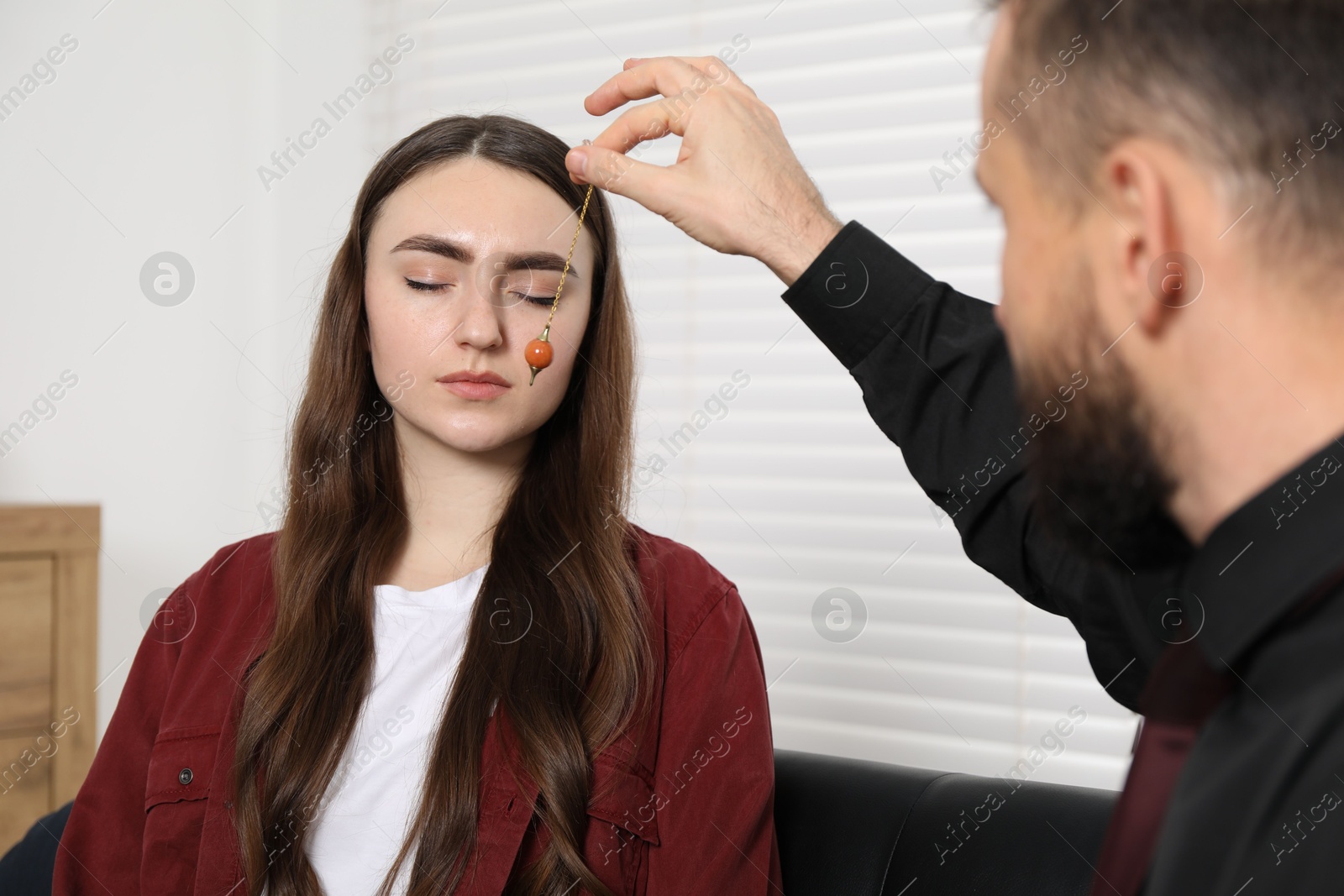 Photo of Psychologist using pendulum while working with patient during hypnosis session indoors