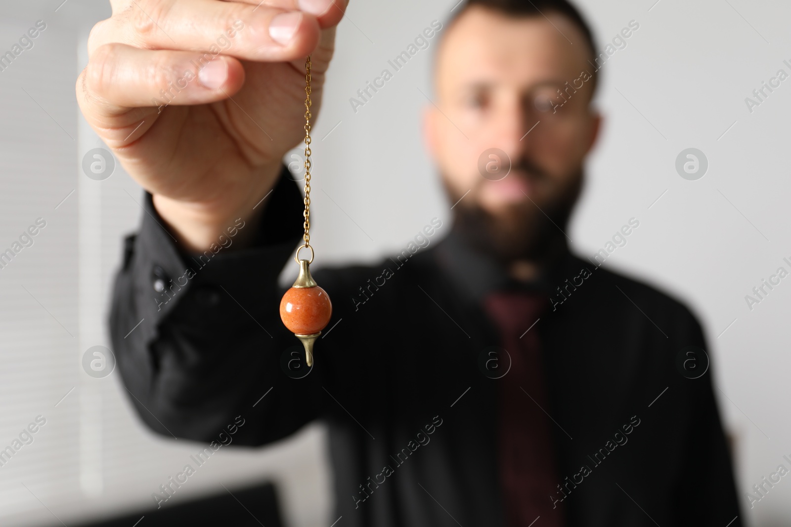 Photo of Hypnosis session. Man with pendulum in office, selective focus