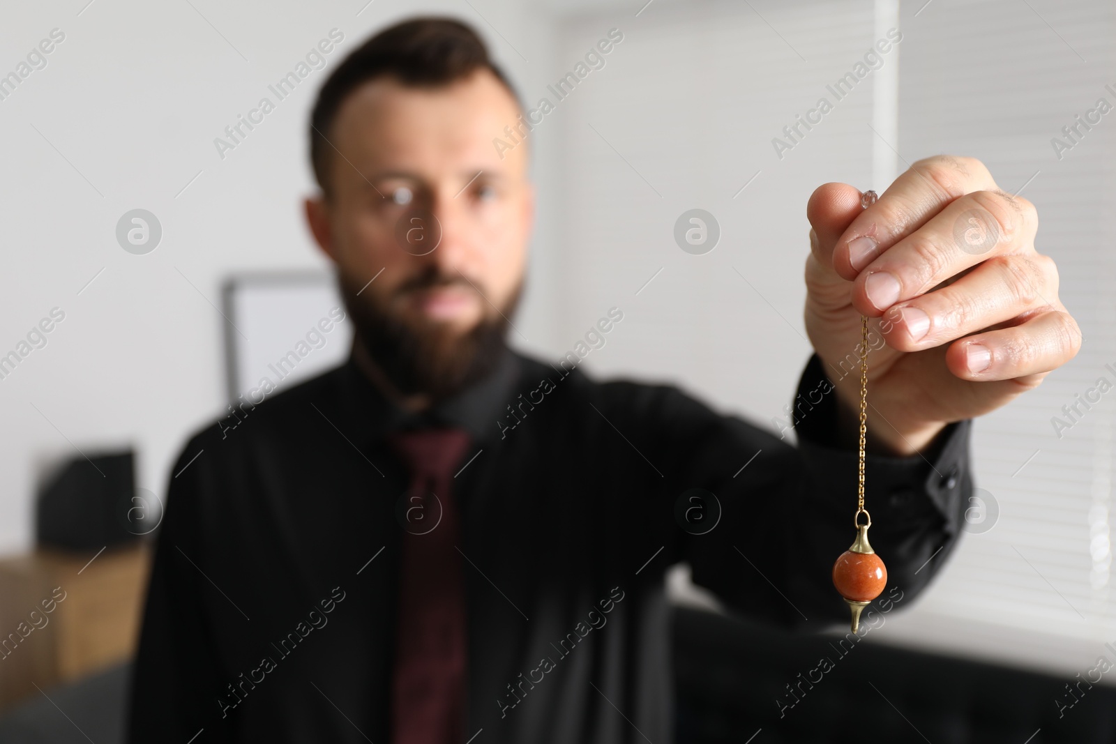 Photo of Hypnosis session. Man with pendulum in office, selective focus