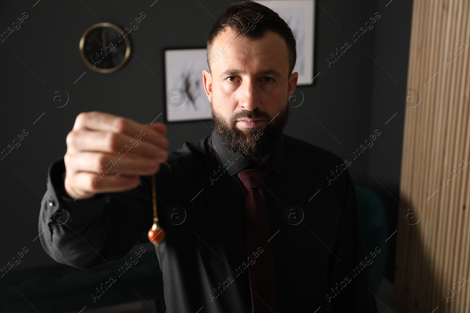 Photo of Hypnosis session. Man with pendulum in office