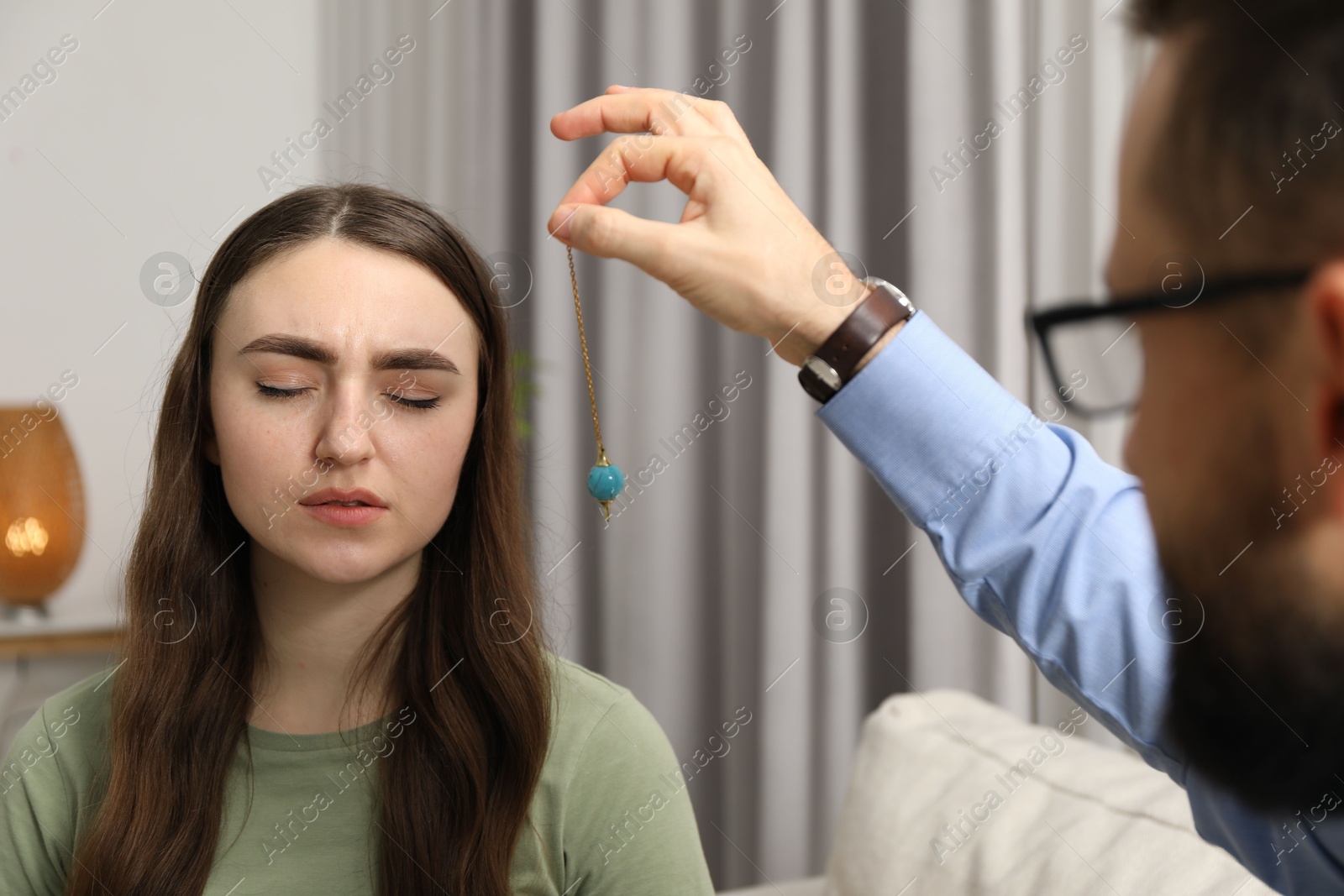 Photo of Psychologist using pendulum while working with patient during hypnosis session indoors, closeup