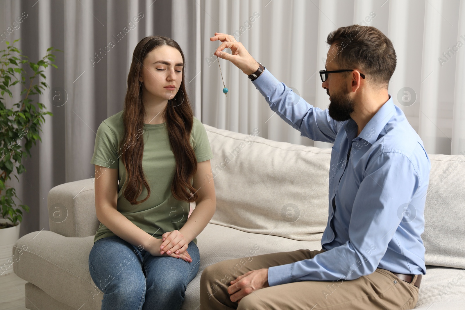 Photo of Psychologist using pendulum while working with patient during hypnosis session indoors