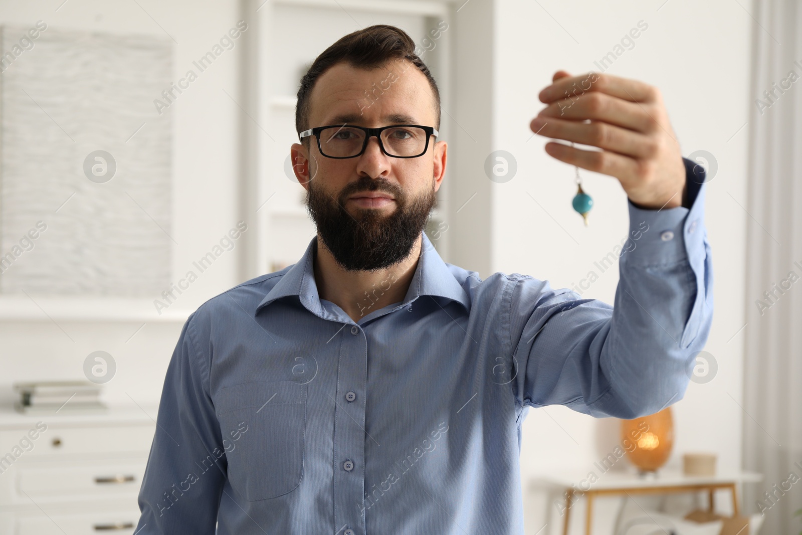 Photo of Hypnosis session. Man in glasses swinging pendulum indoors