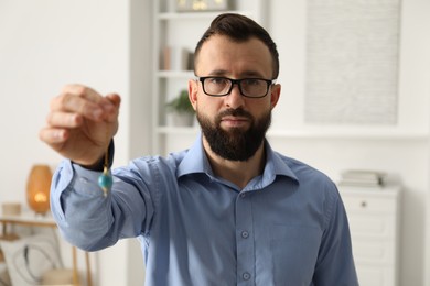 Photo of Hypnosis session. Man in glasses swinging pendulum indoors