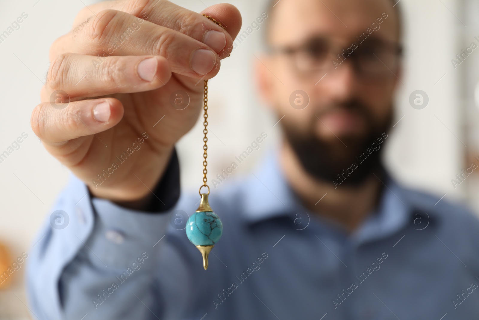 Photo of Hypnosis session. Man with pendulum indoors, selective focus