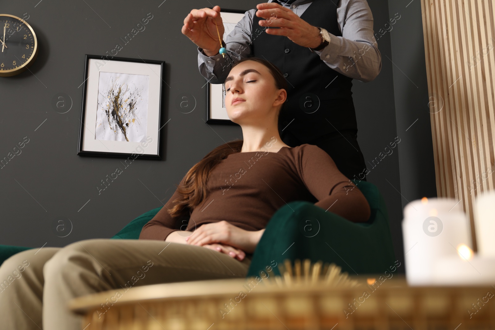 Photo of Psychologist using pendulum while working with patient during hypnosis session indoors, closeup