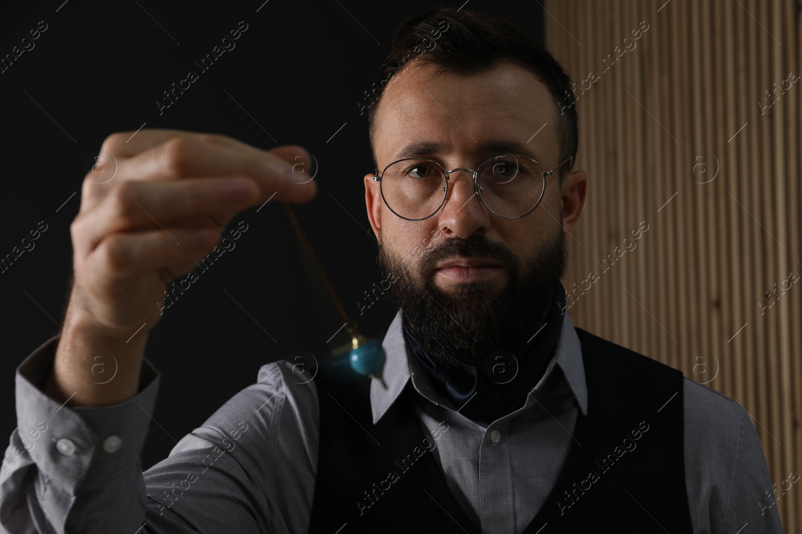 Photo of Hypnosis session. Man in glasses swinging pendulum indoors