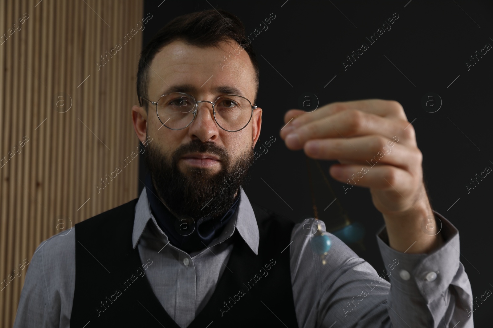 Photo of Hypnosis session. Man in glasses swinging pendulum indoors