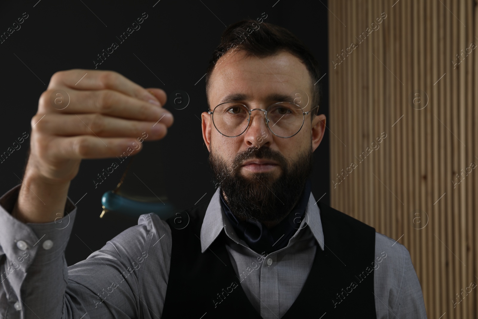 Photo of Hypnosis session. Man in glasses swinging pendulum indoors