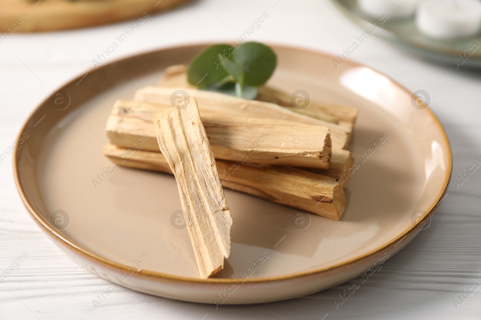 Photo of Palo santo sticks and eucalyptus leaves on white wooden table, closeup