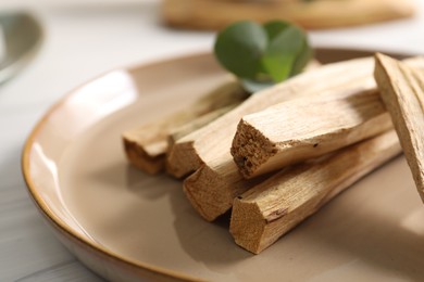 Photo of Palo santo sticks and eucalyptus leaves on white wooden table, closeup