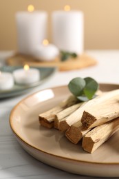 Photo of Palo santo sticks and eucalyptus leaves on white wooden table, closeup