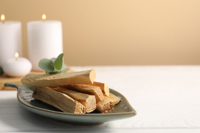 Photo of Palo santo sticks and eucalyptus leaves on white wooden table, closeup. Space for text