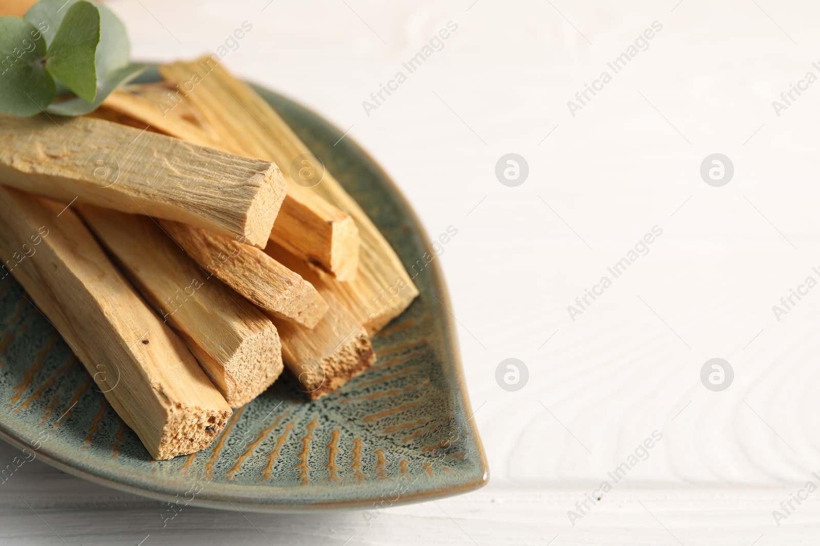 Photo of Palo santo sticks and eucalyptus leaves on white wooden table, closeup. Space for text