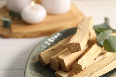 Photo of Palo santo sticks and eucalyptus leaves on white wooden table, closeup