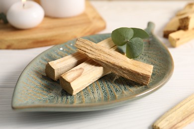 Photo of Palo santo sticks and eucalyptus leaves on white wooden table, closeup