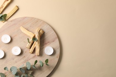 Photo of Palo santo sticks, eucalyptus branches and burning candles on beige background, flat lay. Space for text