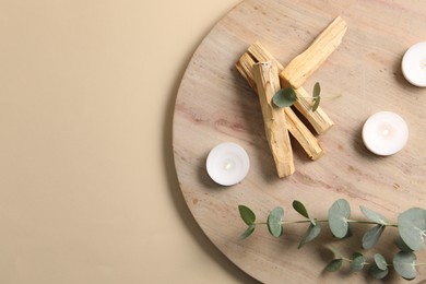 Photo of Palo santo sticks, eucalyptus branches and burning candles on beige background, top view. Space for text