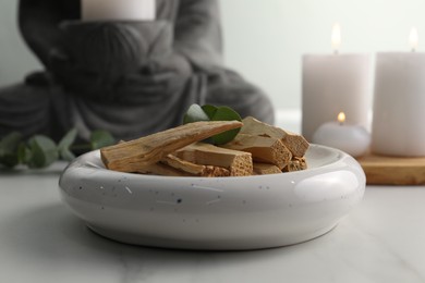 Photo of Palo santo sticks and eucalyptus leaves on white table, closeup