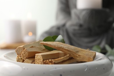 Photo of Palo santo sticks and eucalyptus leaves on blurred background, closeup