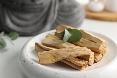 Photo of Palo santo sticks and eucalyptus leaves on white table, closeup