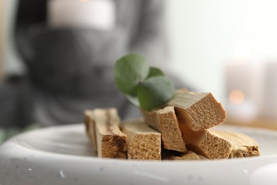 Photo of Palo santo sticks and eucalyptus leaves on blurred background, closeup