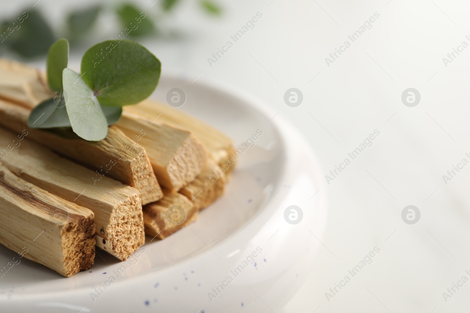 Photo of Palo santo sticks and eucalyptus leaves on white table, closeup. Space for text