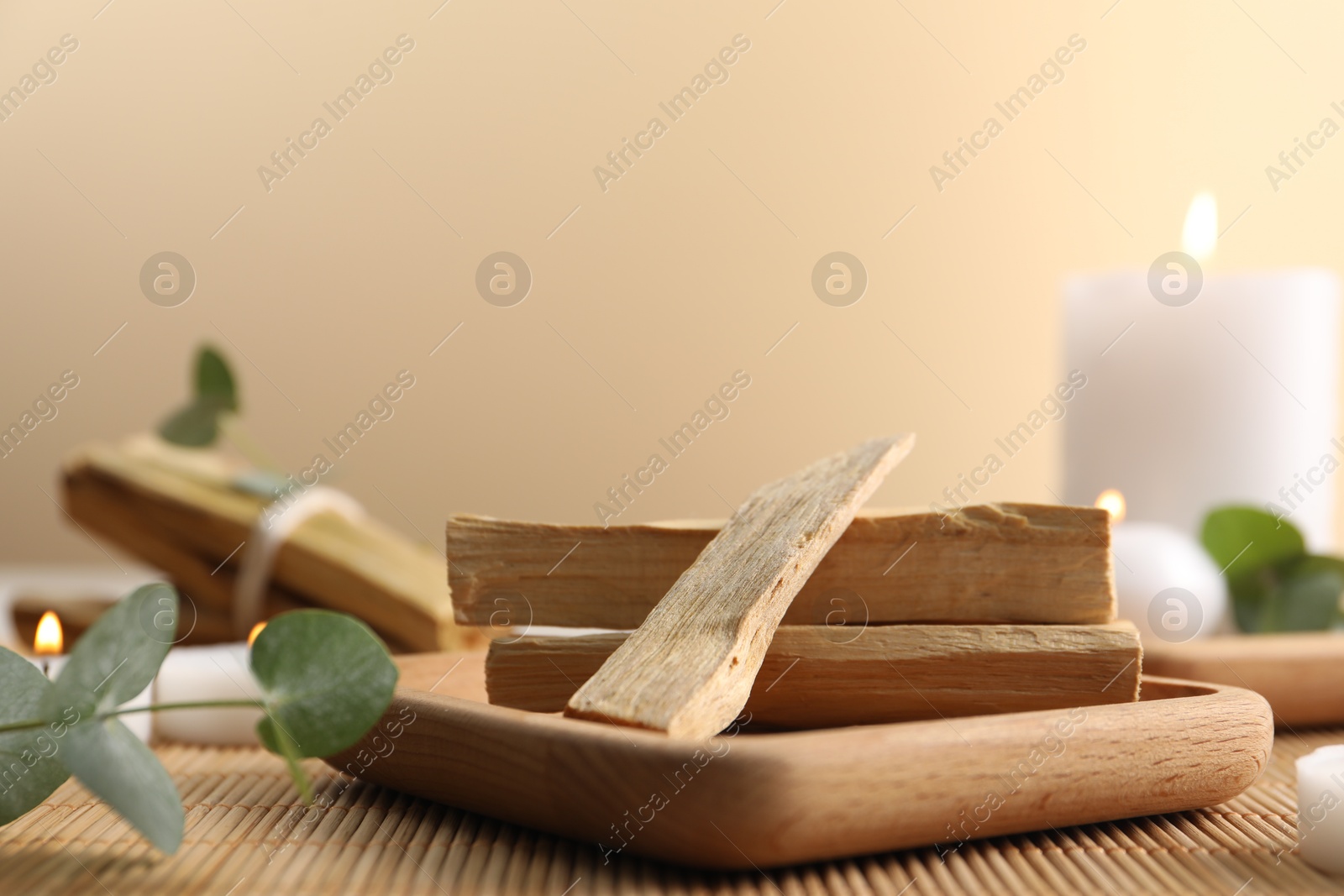 Photo of Palo santo sticks, eucalyptus branches and burning candles on bamboo mat, closeup