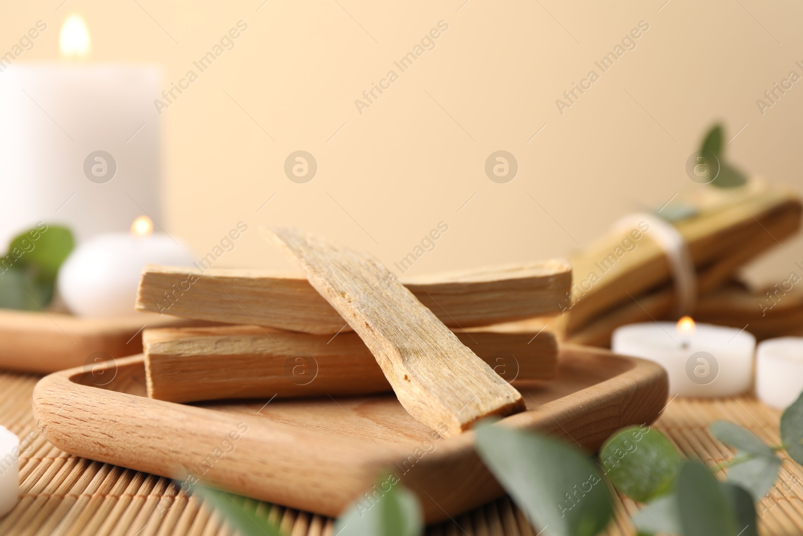 Photo of Palo santo sticks, eucalyptus branches and burning candles on bamboo mat, closeup