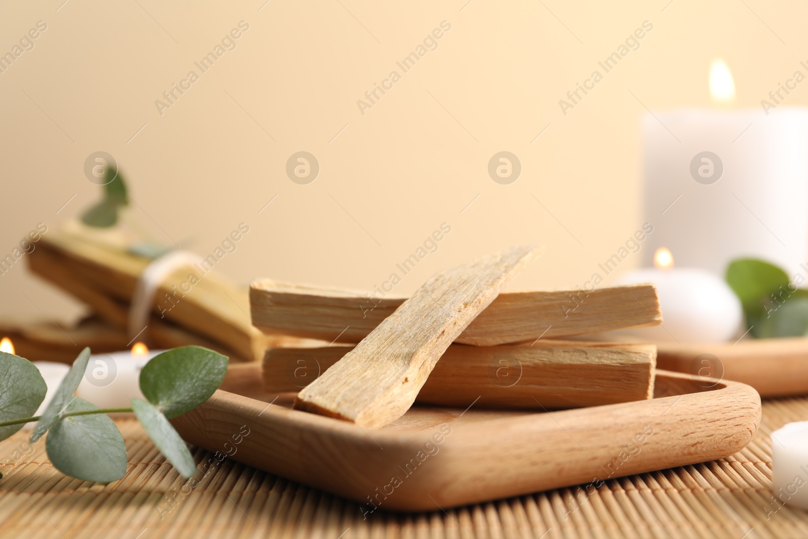 Photo of Palo santo sticks, eucalyptus branches and burning candles on bamboo mat, closeup