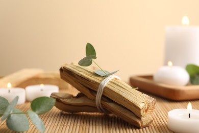 Photo of Palo santo sticks, eucalyptus branches and burning candles on bamboo mat, closeup